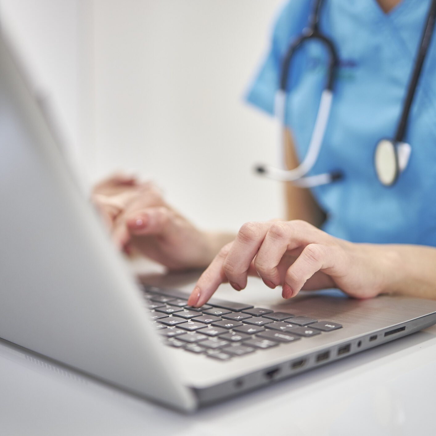 Close-up hands of unrecognizable female physician in medical uniform working typing on laptop keyboard sitting at desk Close-up hands of unrecognizable female physician in medical uniform working typing on laptop keyboard sitting at desk